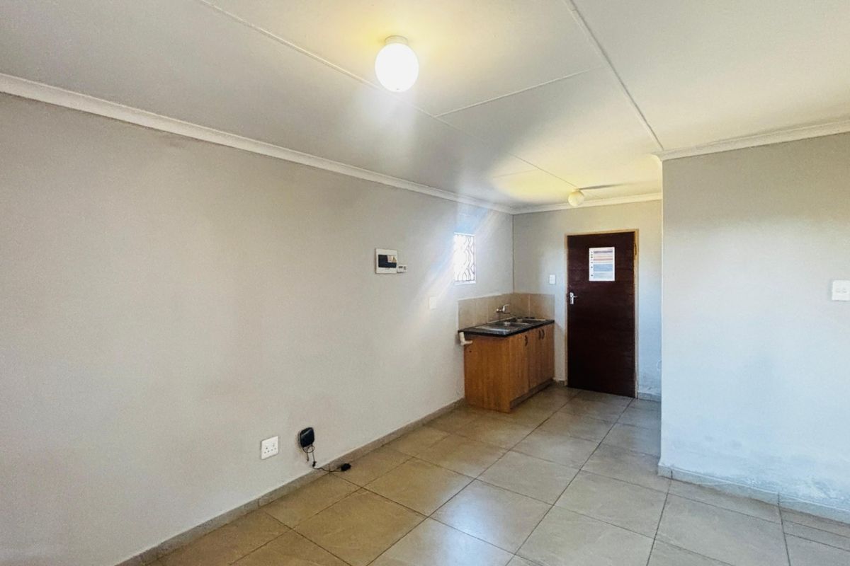 A compact, empty kitchen area featuring tiled flooring, base cabinetry with a sink, and neutral wall finishes.