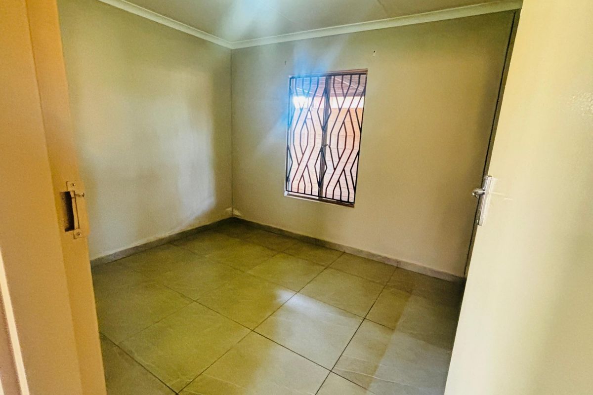An empty bedroom featuring tiled flooring and a window fitted with security bars.