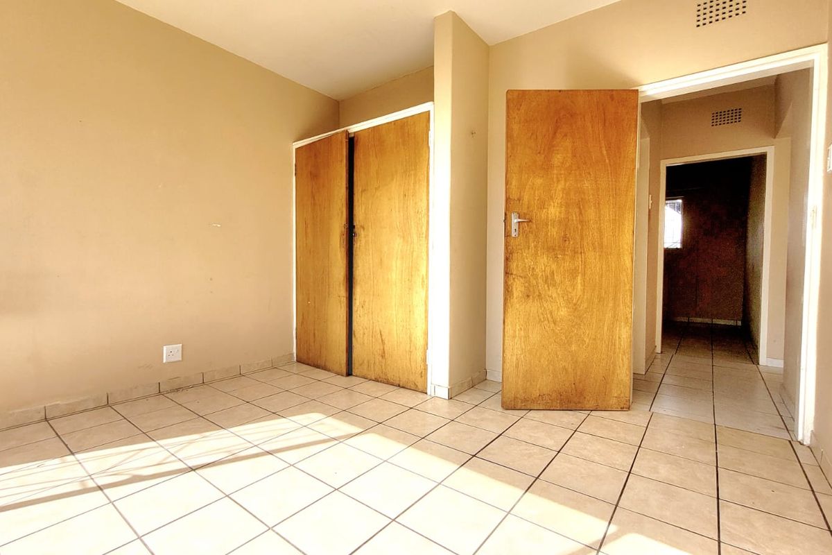 An empty bedroom featuring tiled flooring and built-in wooden cupboards, offering a blank canvas for renovation or interior design updates.