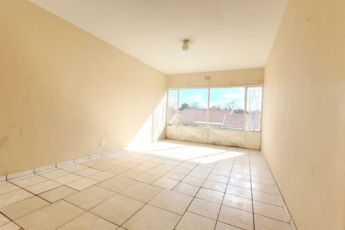 A bright, empty living room featuring tiled flooring and large windows, offering a blank canvas ready for personalization and renovation.