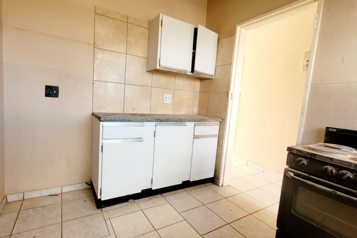 A compact kitchen area featuring basic built-in cabinetry, stone countertops, tiled backsplash, and tiled flooring, ready for modernization.