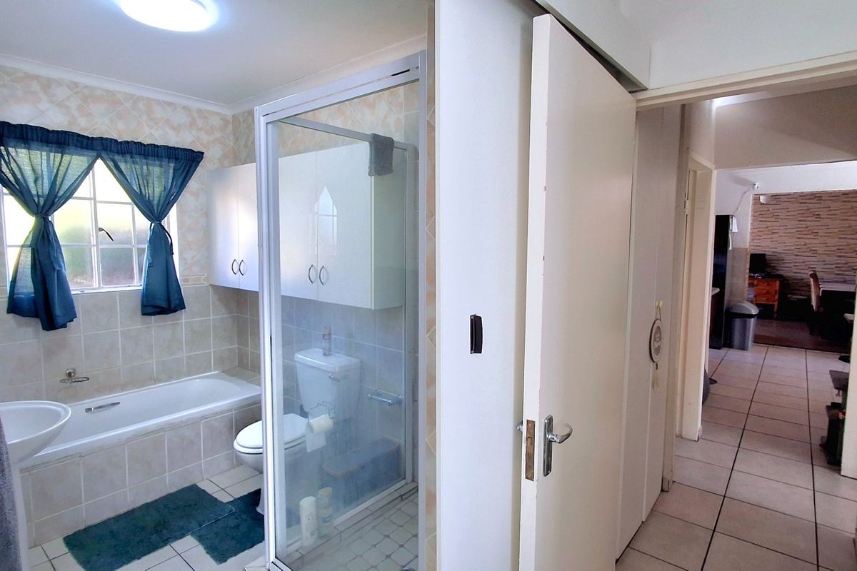 A functional bathroom featuring a bathtub, separate shower enclosure, toilet, and wall-mounted cabinetry with neutral tiled finishes.