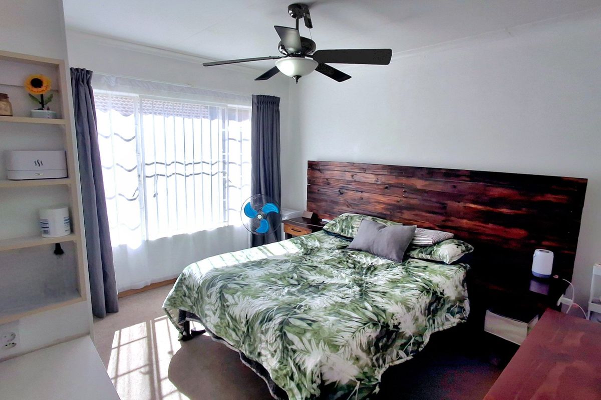 A bedroom featuring a ceiling fan, built-in shelving unit, and a window fitted with security bars.