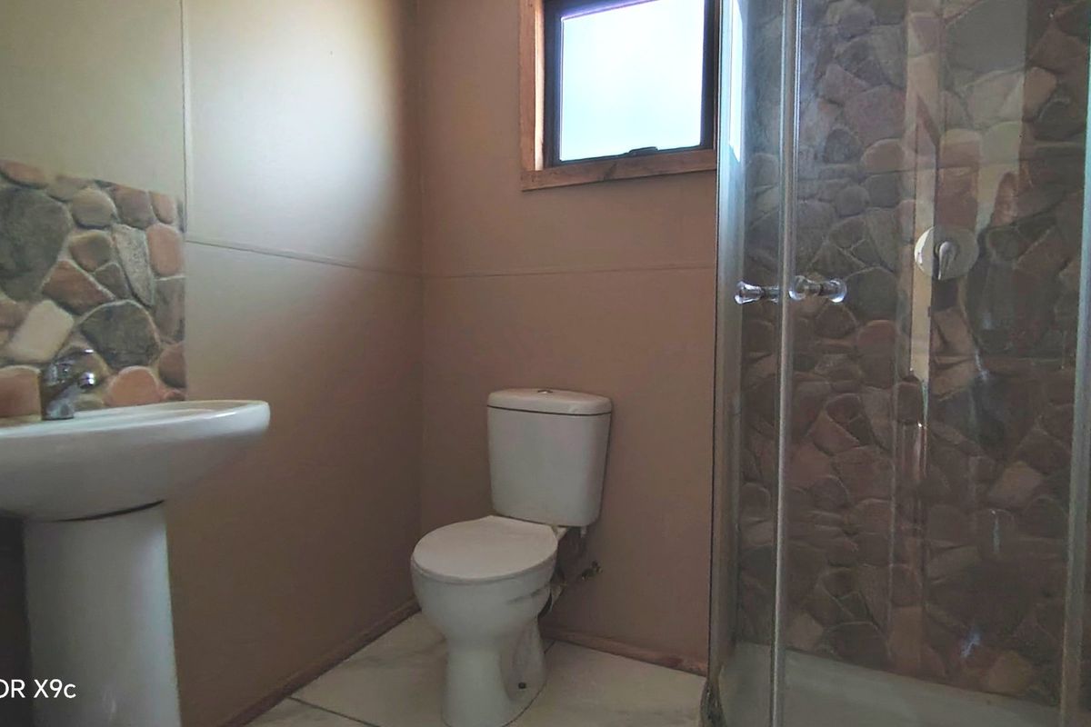 A functional bathroom featuring a pedestal basin, toilet, and a shower enclosure with decorative stone-cladding accents.