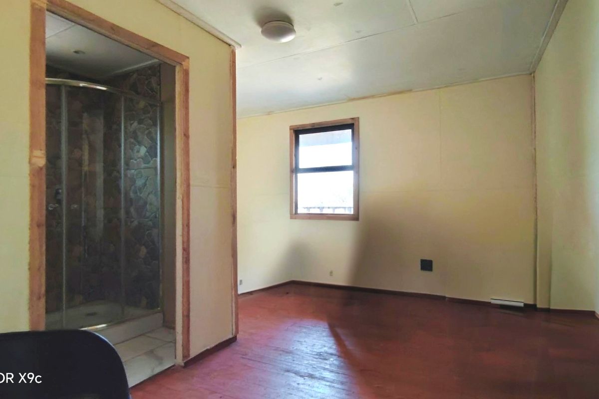An empty bedroom featuring timber flooring and an attached en-suite shower area with unfinished door framing and visible wall paneling.