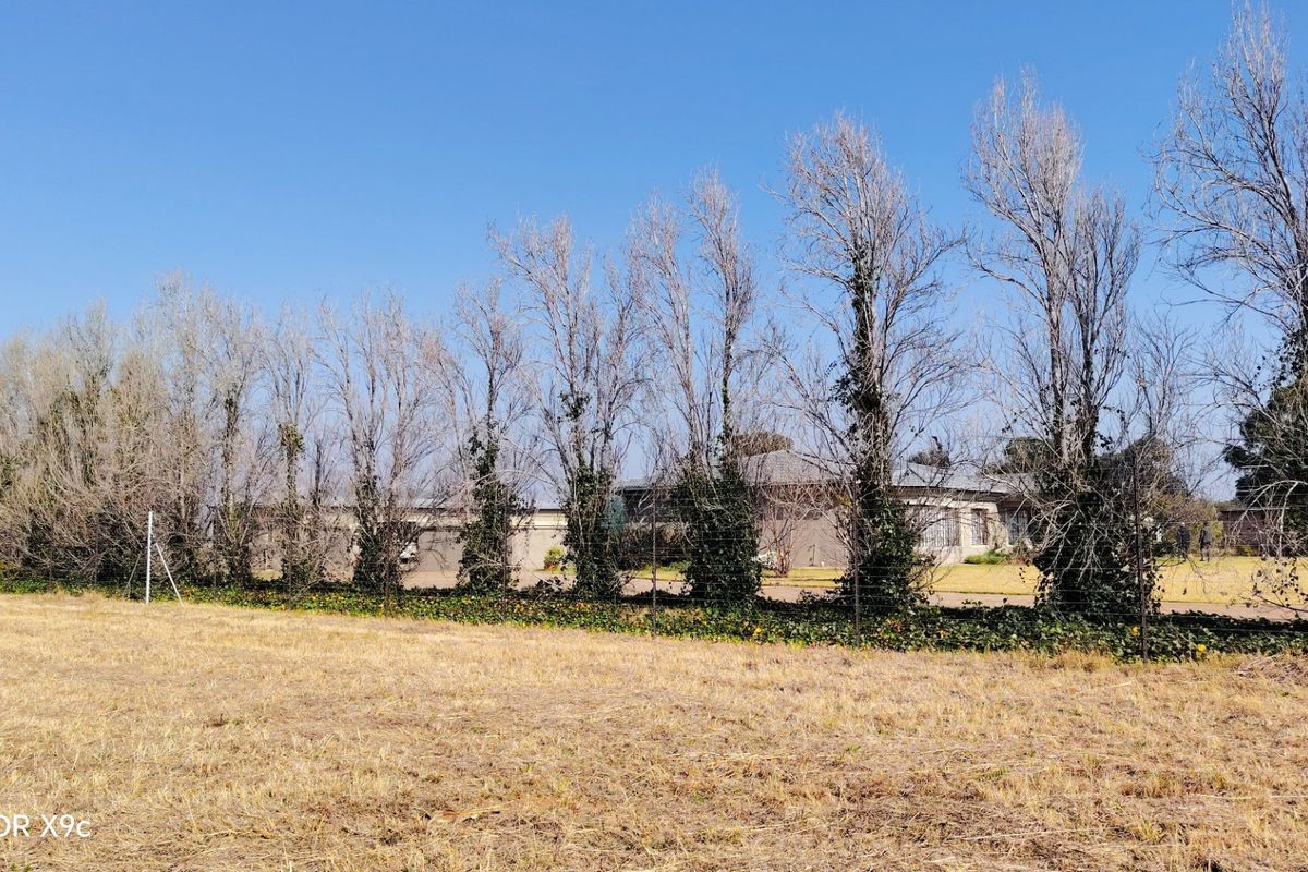 A view of the property exterior from the rear, featuring established trees, wire fencing, and a glimpse of the main dwelling structure.