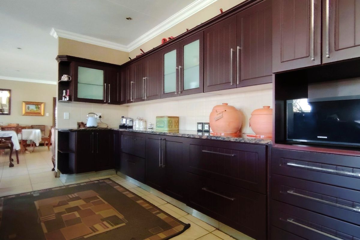 A functional kitchen featuring dark wood cabinetry, granite countertops, and built-in microwave, with an open-plan layout leading to the dining area.