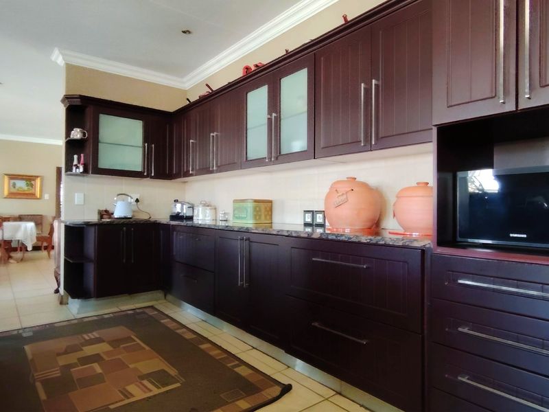 A functional kitchen featuring dark wood cabinetry, granite countertops, and built-in microwave, with an open-plan layout leading to the dining area.