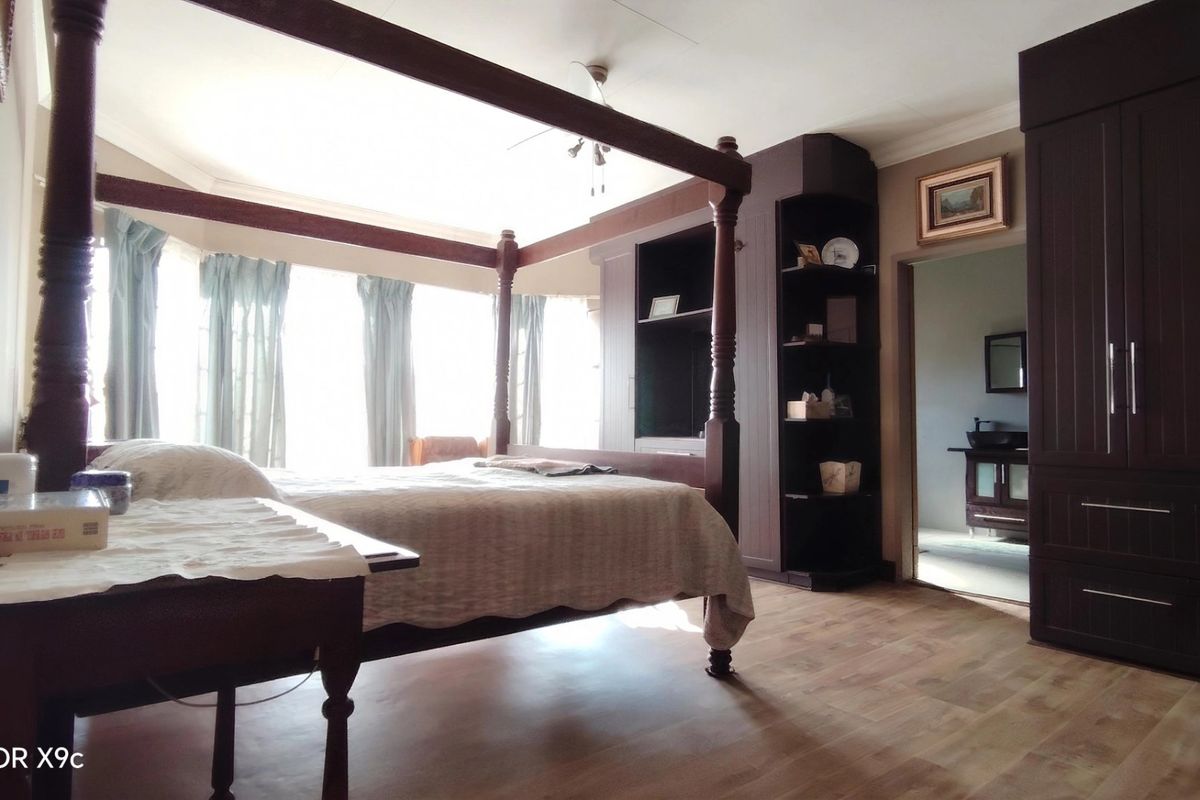 Spacious bedroom featuring laminate flooring, built-in dark wood cabinetry, and a bay window, with an adjoining en-suite bathroom visible.