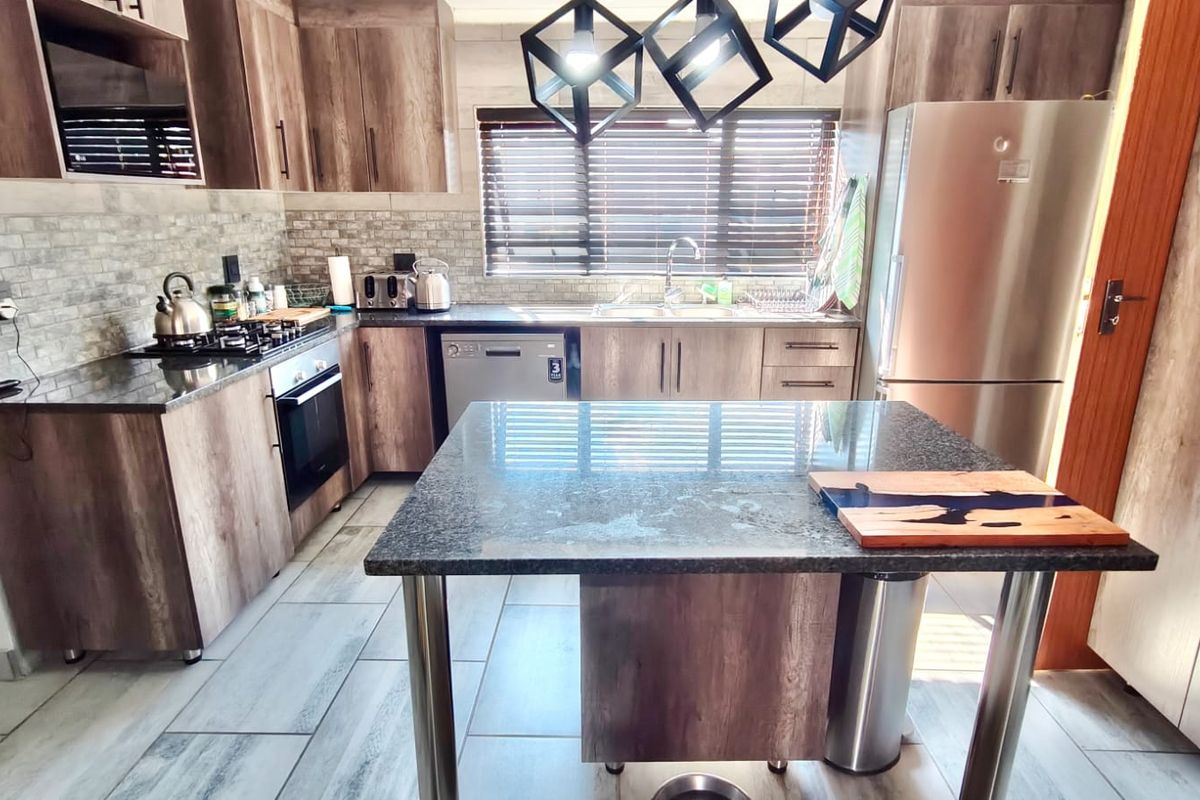 Modern kitchen featuring wood-look cabinetry, granite countertops, a central island, and integrated appliances, offering a functional and contemporary cooking space.