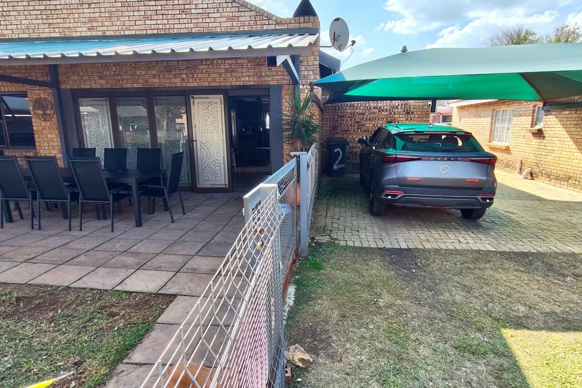 Rear exterior view featuring a paved patio area, brick facade, and a covered driveway with a shade sail structure.