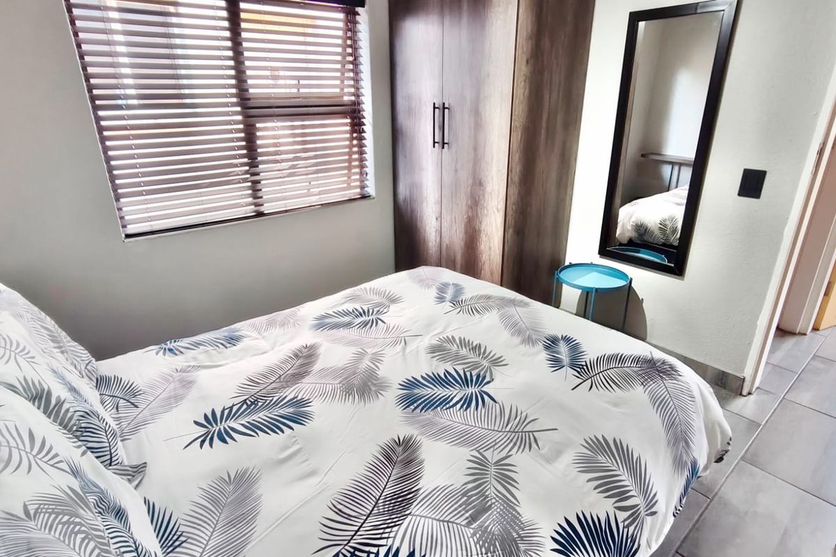A well-lit bedroom featuring a built-in wardrobe, tiled flooring, and venetian blinds, providing a functional and comfortable living space.