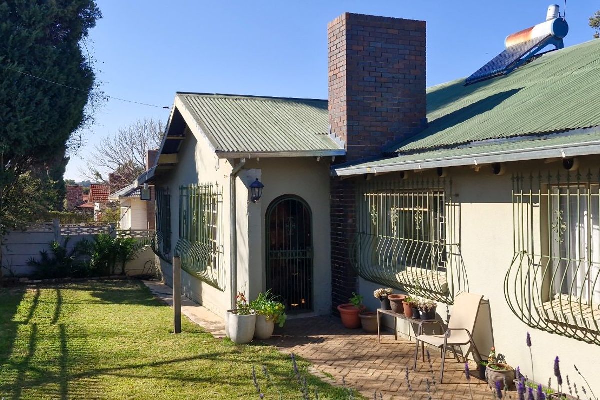 Rear exterior view of the house featuring a corrugated metal roof, brick chimney, solar water heater, and a paved patio area with security bars.