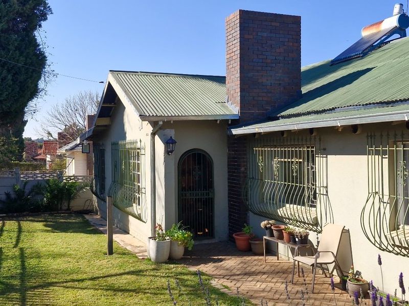 Rear exterior view of the house featuring a corrugated metal roof, brick chimney, solar water heater, and a paved patio area with security bars.