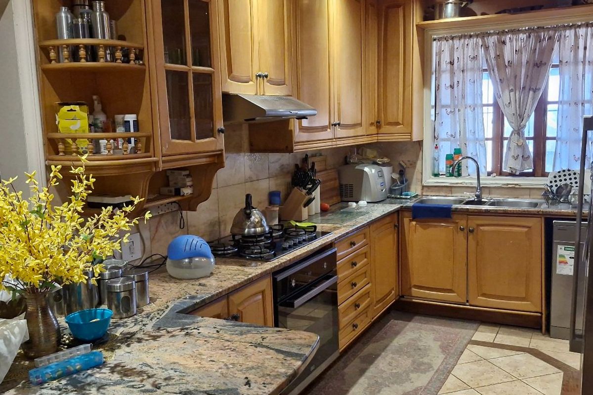 A functional kitchen featuring wooden cabinetry, granite countertops, a gas hob, and a tiled backsplash, offering a classic layout with ample storage space.