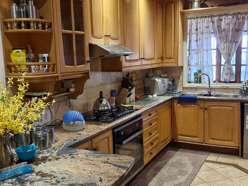 A functional kitchen featuring wooden cabinetry, granite countertops, a gas hob, and a tiled backsplash, offering a classic layout with ample storage space.