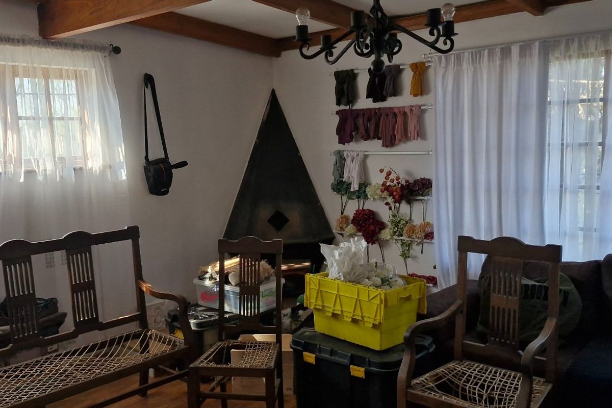 A living room featuring exposed timber ceiling beams, a corner fireplace, and a wrought iron chandelier, offering a rustic aesthetic with natural light.