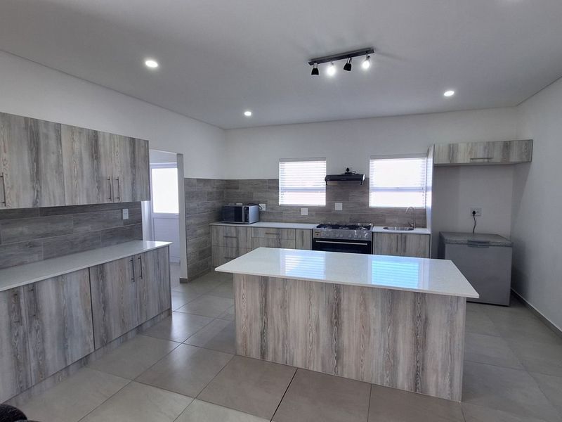 Modern kitchen featuring light wood-grain cabinetry, stone countertops, a central island, gas stove, and tiled flooring with recessed lighting.