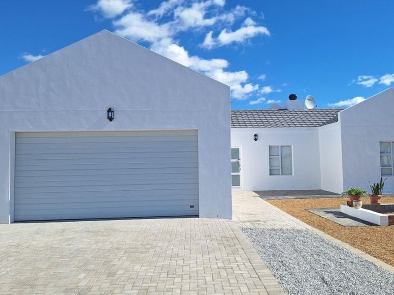 A well-maintained single-story house featuring a white facade, a double garage, paved driveway, and neat gravel landscaping under a clear blue sky.