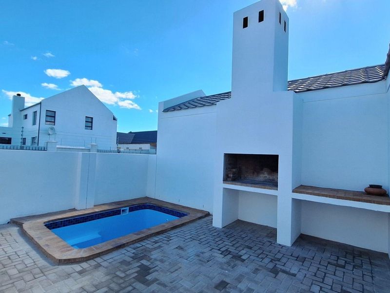 Outdoor entertainment area featuring a paved patio, a built-in braai with chimney, and a private swimming pool.
