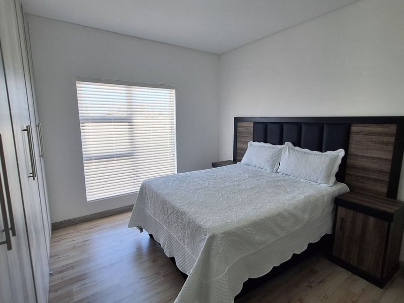 A well-maintained bedroom featuring laminate flooring, built-in cupboards, and a custom integrated headboard with matching bedside tables.