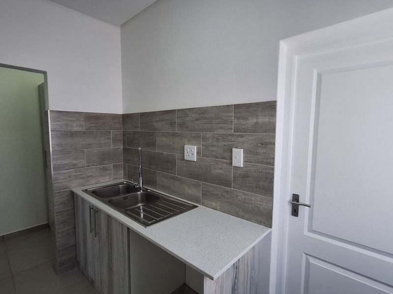 A clean and modern scullery area featuring a stainless steel double sink, stone countertop, and wood-look tile backsplash with ample built-in cabinetry.