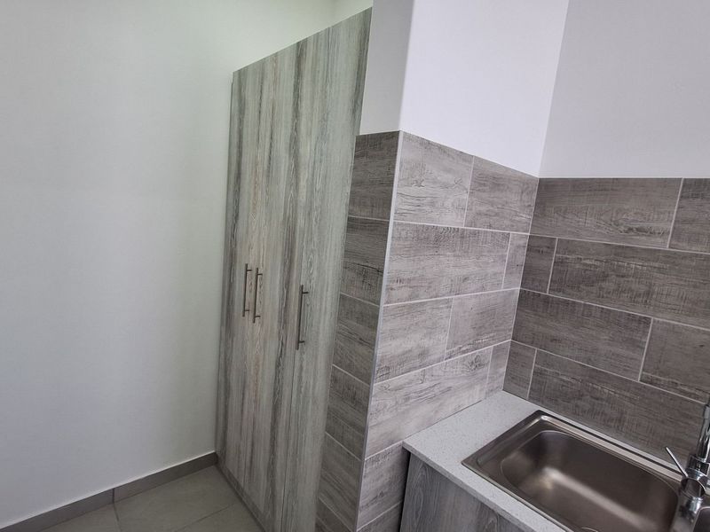A clean and modern scullery featuring wood-look cabinetry, a stainless steel sink, and matching tiled splashback.