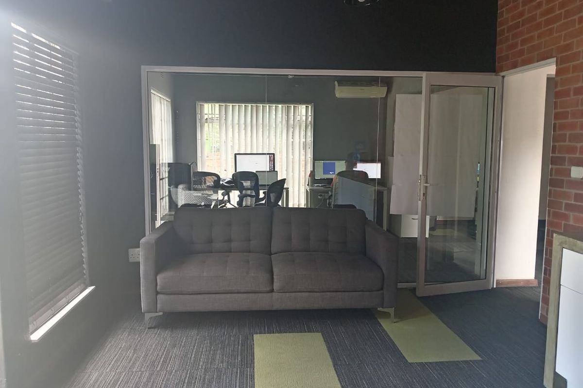 A modern office space featuring a glass partition wall, exposed brick accents, and carpeted flooring, creating a professional and contemporary work environment.