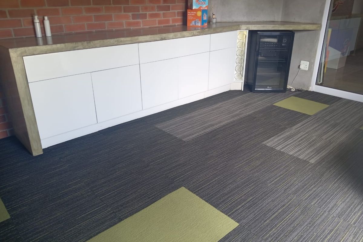Modern office space featuring built-in white cabinetry with a concrete countertop, exposed brick wall, and patterned carpet tiles.