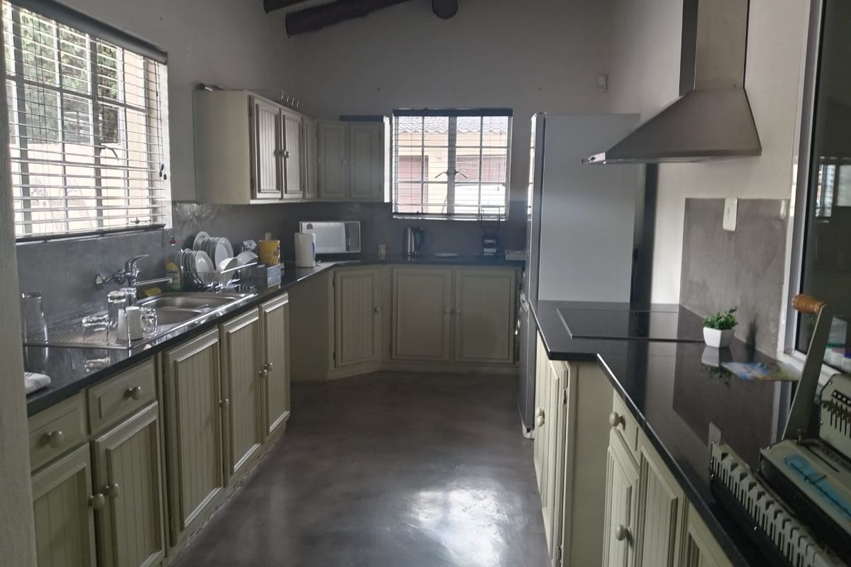 A functional kitchen featuring built-in cabinetry, granite countertops, stainless steel sink, extractor fan, and exposed timber ceiling beams.