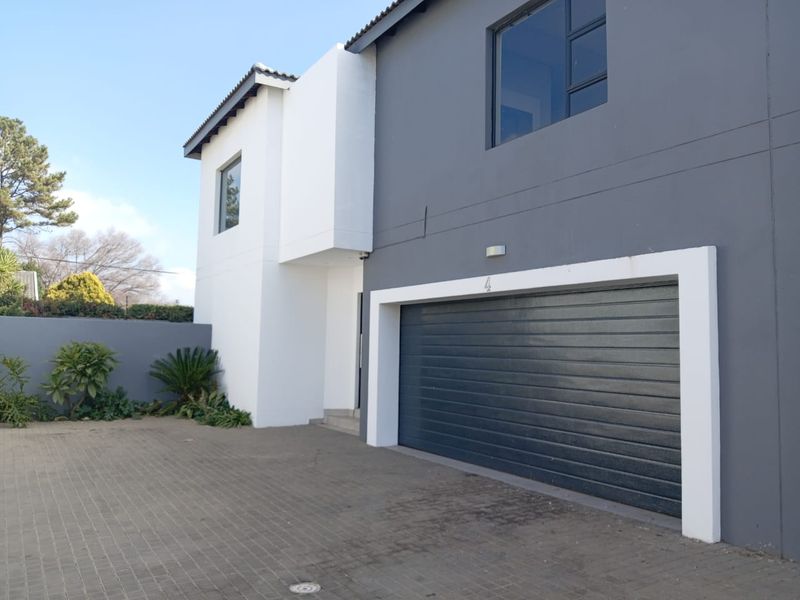 Modern townhouse exterior featuring a paved driveway, automated garage door, and contemporary two-tone facade with clean architectural lines.