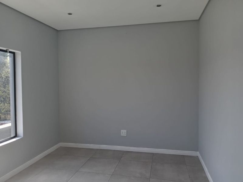 A clean, empty bedroom featuring neutral grey walls, tiled flooring, and recessed downlighting, providing a versatile space ready for personalization.