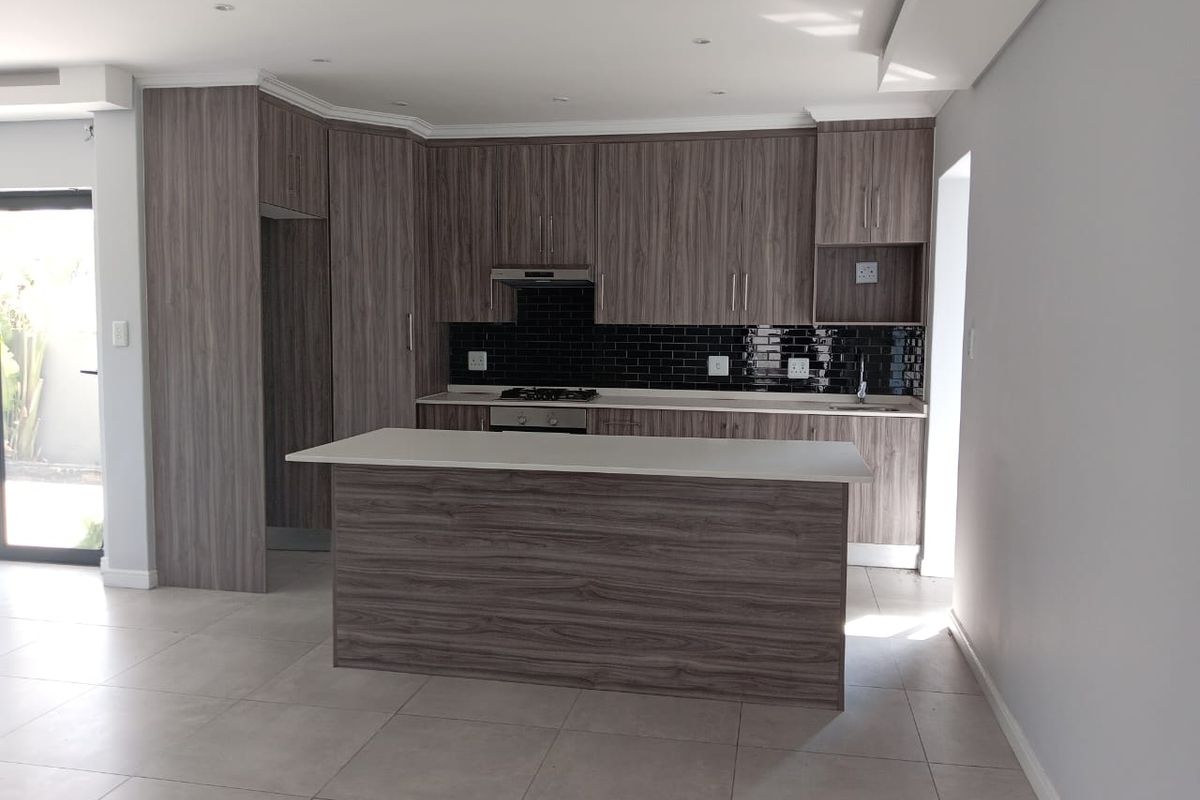 Modern kitchen featuring wood-grain cabinetry, a central island, gas hob, extractor fan, and sleek subway tile backsplash in an open-plan layout.