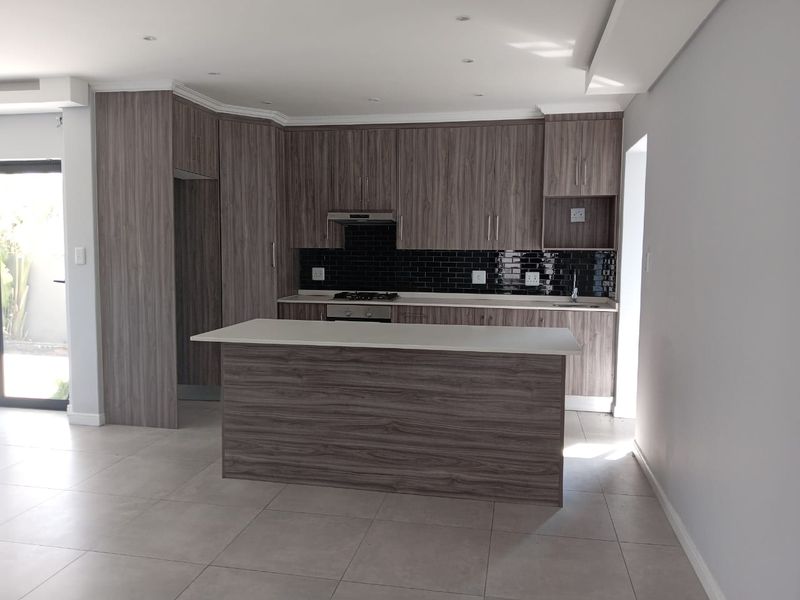 Modern kitchen featuring wood-grain cabinetry, a central island, gas hob, extractor fan, and sleek subway tile backsplash in an open-plan layout.
