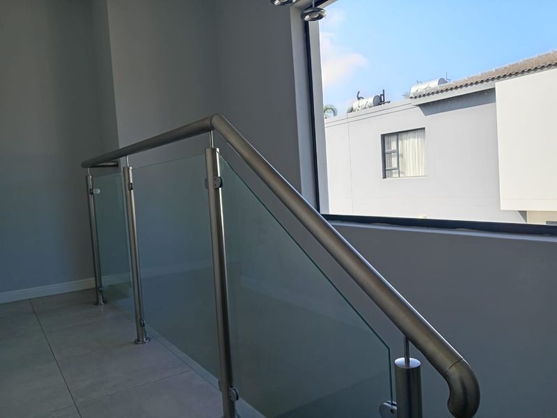A bright hallway landing featuring a modern stainless steel and glass balustrade with large windows overlooking the neighboring property.