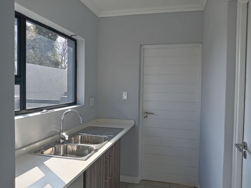 A clean and modern scullery featuring a double bowl stainless steel sink, stone countertops, and built-in cabinetry, finished with neutral grey walls.