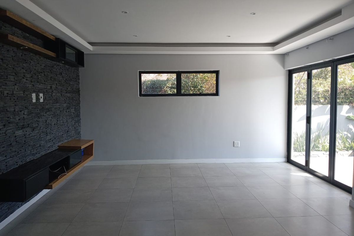 Spacious living area featuring a modern stacked stone feature wall, built-in floating cabinetry, recessed ceiling lighting, and large aluminium folding doors leading outdoors.