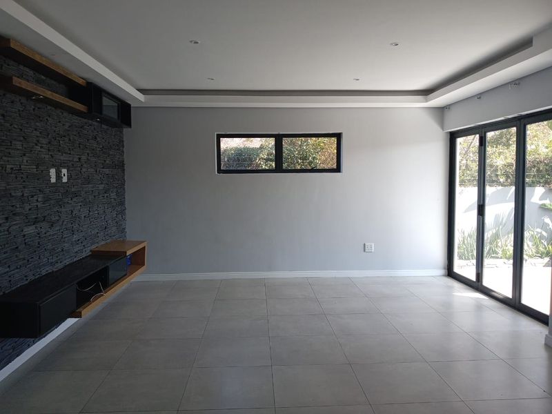 Spacious living area featuring a modern stacked stone feature wall, built-in floating cabinetry, recessed ceiling lighting, and large aluminium folding doors leading outdoors.