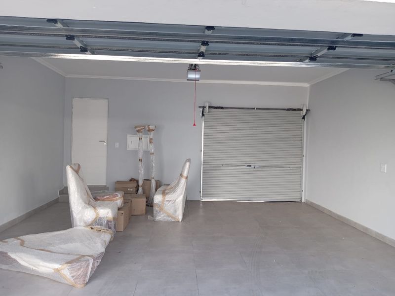 A clean, spacious double garage featuring tiled flooring, a sectional overhead door, and an additional internal roller shutter door for secure access.
