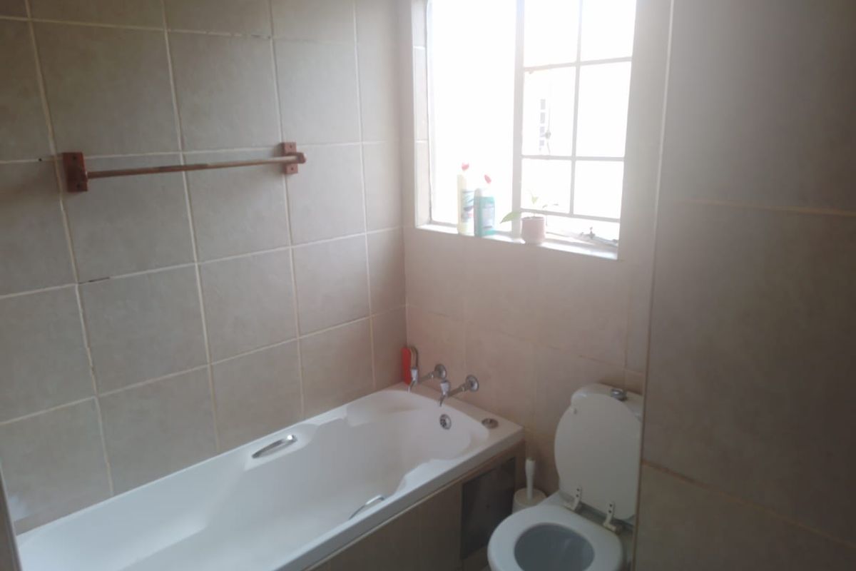 A functional bathroom featuring a built-in bathtub, toilet, and tiled wall finishes, illuminated by natural light from a window.