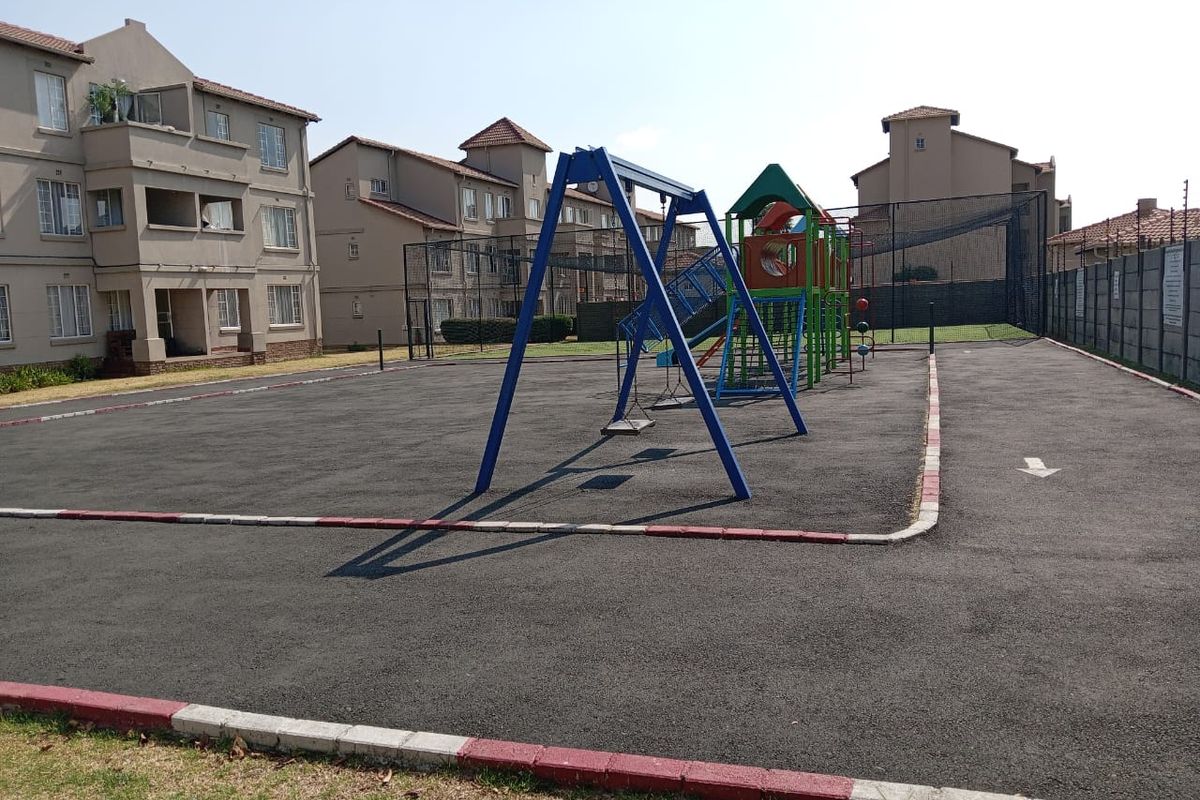 Communal outdoor area featuring an asphalt playground with fixed play equipment, situated within a residential apartment complex.