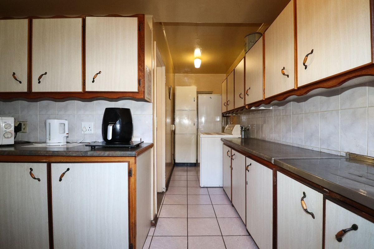 A galley-style kitchen featuring dated laminate cabinetry, tiled backsplash, and tiled flooring, offering a functional layout ready for modernization.