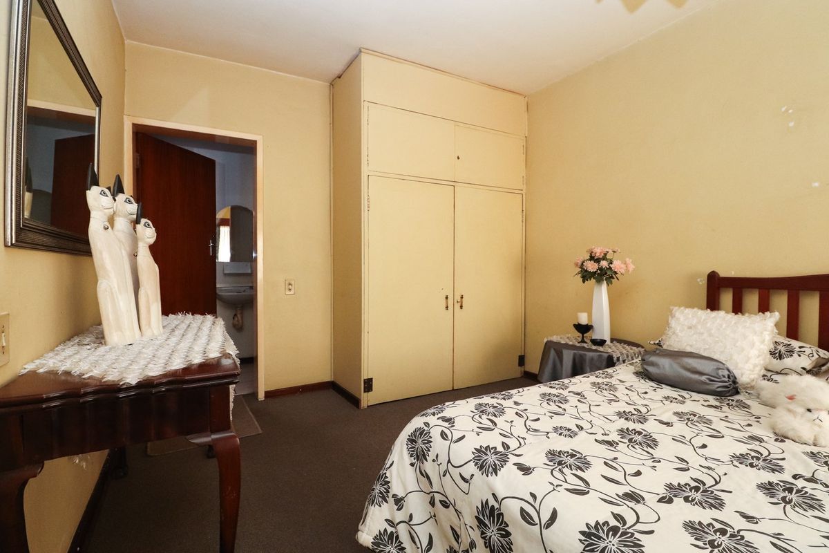 A bedroom featuring built-in wardrobe storage and carpeted flooring, with an adjacent view into a small bathroom area.