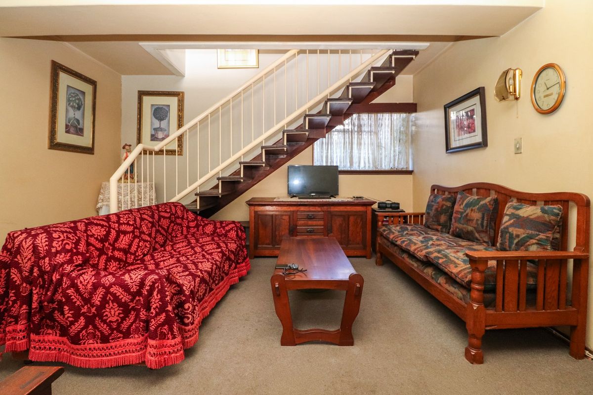 A living room featuring a central staircase with a metal balustrade and carpeted flooring, offering a functional layout with potential for modernization.