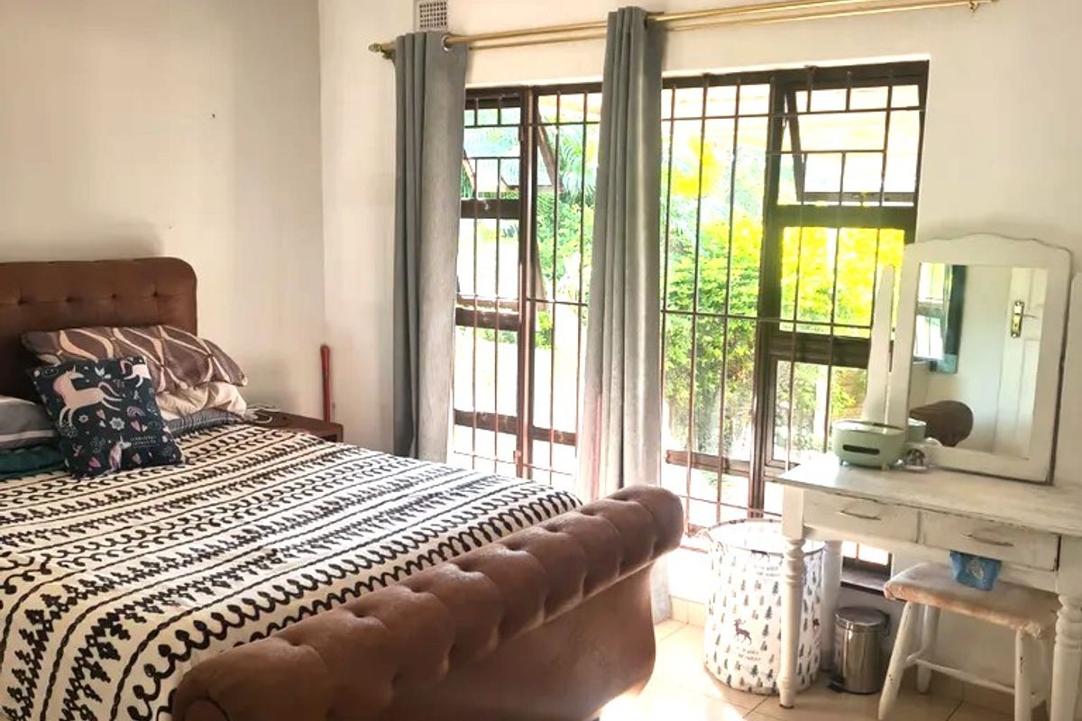 A bedroom featuring tiled flooring, a large window with security bars, and direct access to the garden area.