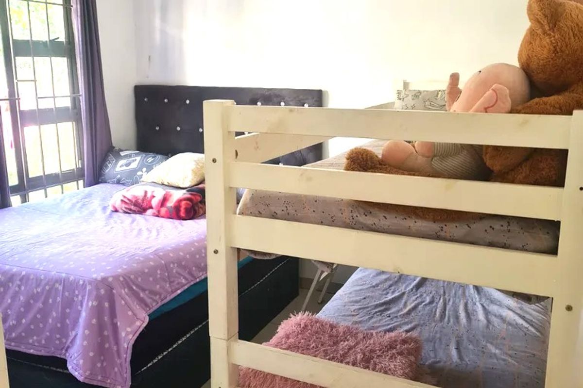 A functional bedroom featuring tiled flooring and a window with security burglar bars, providing a practical space for sleeping arrangements.