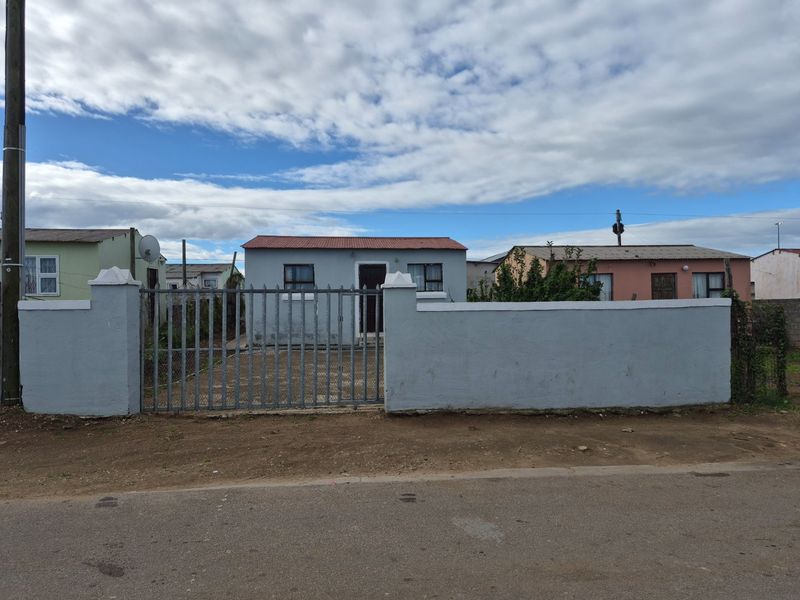 Front view of a single-story house featuring a perimeter wall, metal security gate, and a paved driveway area.