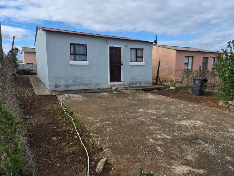A detached single-story house featuring a concrete driveway, corrugated metal roof, and security gate, requiring exterior maintenance and landscaping improvements.