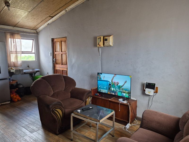 Open plan living area featuring tiled flooring, exposed beam ceiling, and a compact kitchen sink area.