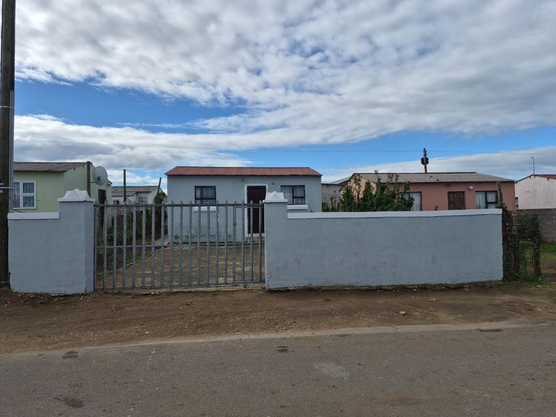 Front view of a single-story house featuring a metal perimeter fence, gated entrance, and a corrugated metal roof.